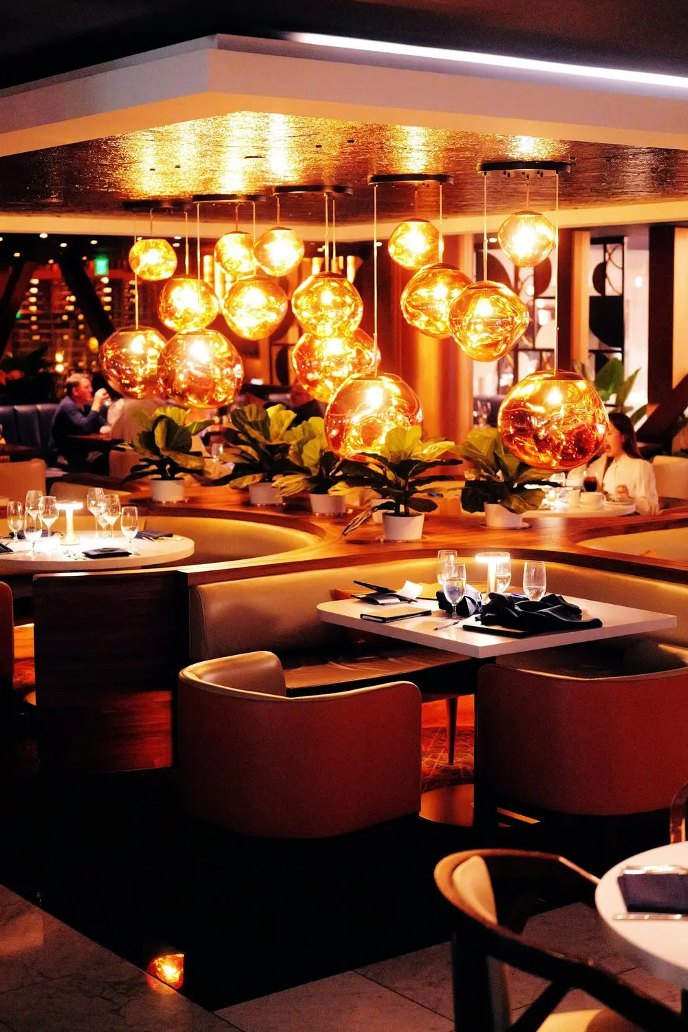 Comedor de restaurante con gabinetes y mesas puestas bajo lámparas colgantes de luz cálida