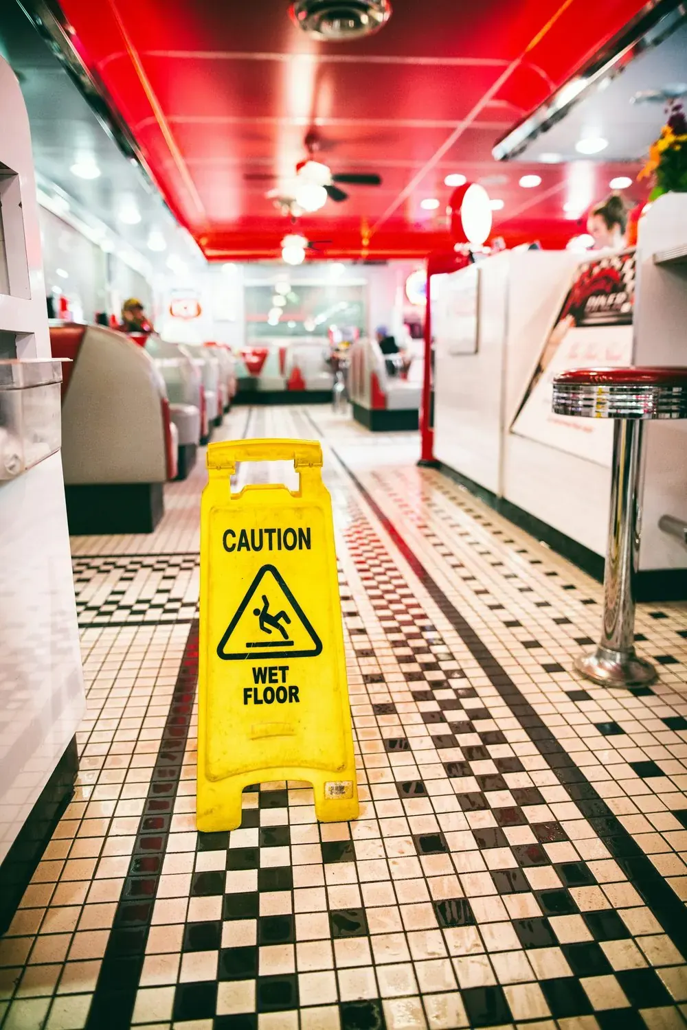 Letrero amarillo de piso mojado sobre un piso de mosaico recién trapeado en un restaurante
