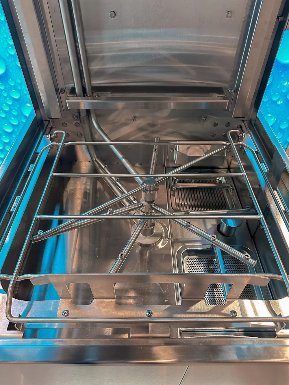 Interior de una máquina lavaplatos comercial con los brazos de lavado y la guía de canastillas